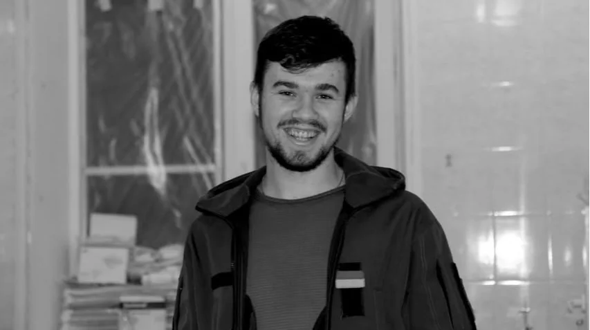 Молодий чоловік з бородою у куртці посміхається на чорно-білому портреті