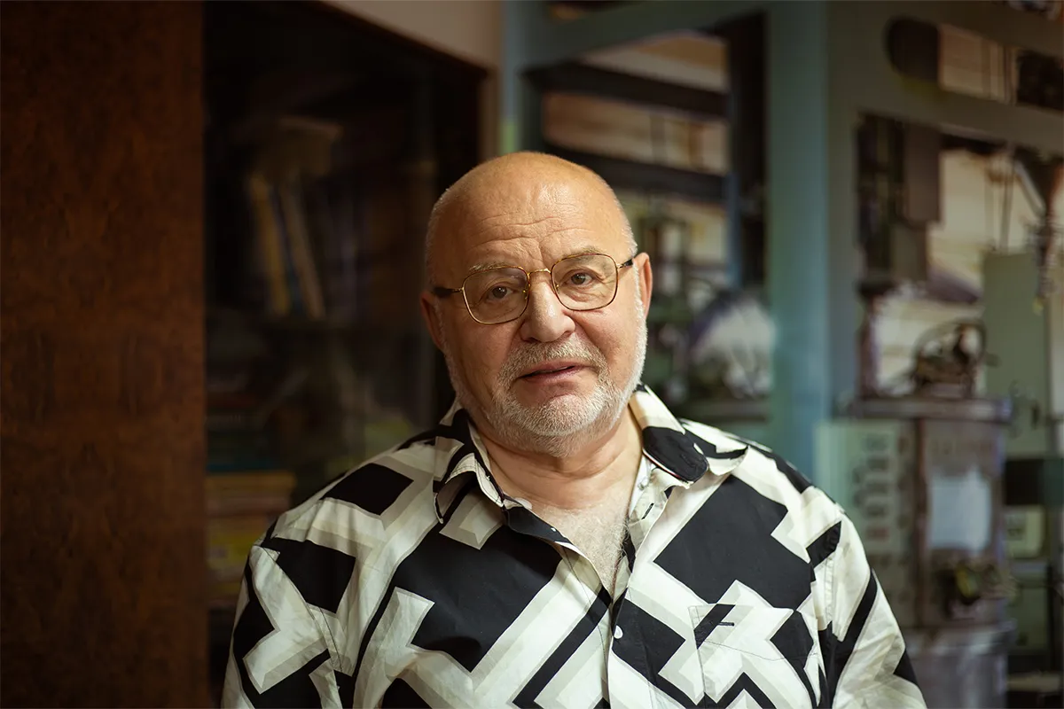 Портрет Бориса Гриньова в окулярах і сорочці з геометричним візерунком на тлі майстерні